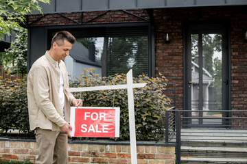 Wall Mural - real estate agent hanging signboard with for sale lettering near modern cottage in city