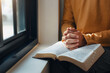 © Kannapat - A man hands folded holy bible by the window in library and church