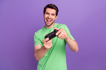 Photo of cheerful pleasant man with stubble dressed green t-shirt hold joystick play excited game isolated on purple color background