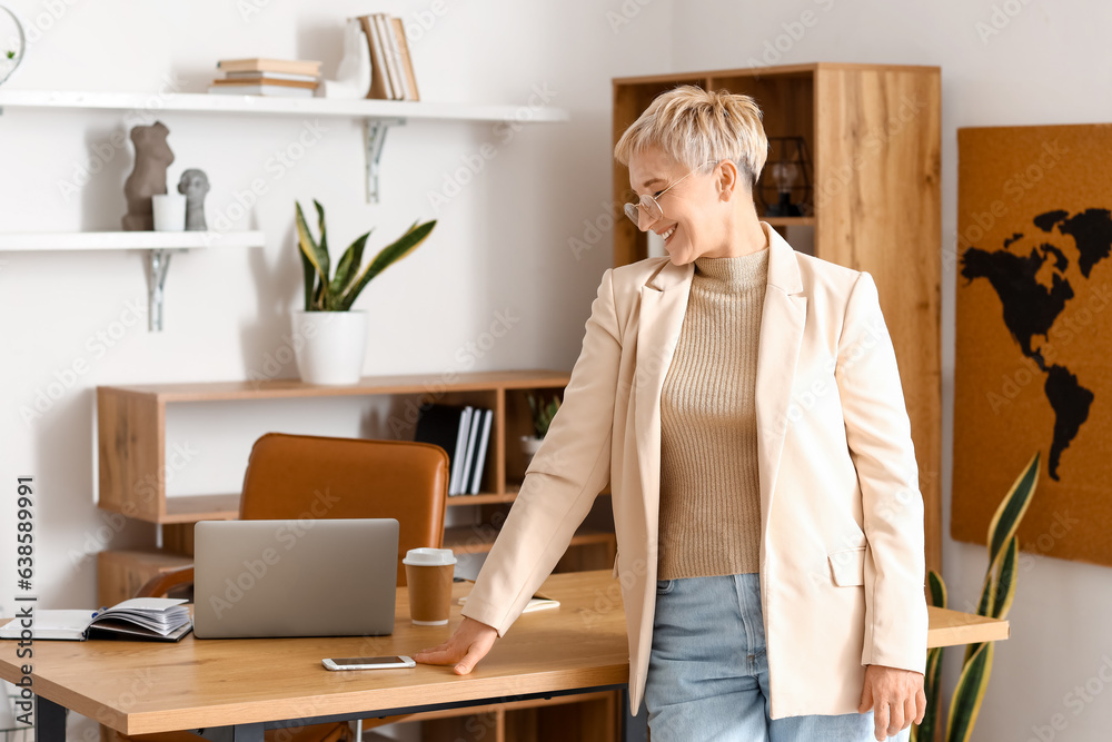 Mature businesswoman near table in office