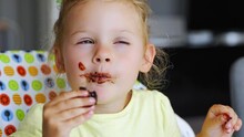 Little Girl With Blond Hair Eating Homemade Chocolate With Dirty Mouth And Hands In Home Kitchen