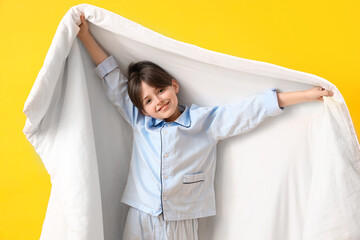 Cute little boy with blanket on yellow background