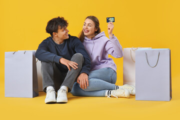 Wall Mural - Happy young couple with credit card and shopping bags sitting on yellow background