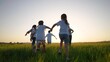 © maxximmm - a group of children run across the field on the grass. happy family kid lifestyle dream concept. children running in a field with tall grass on the sunset. girls holding hands in the foreground