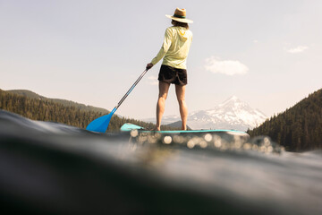 Wall Mural - A young woman cools off in an alpine lake at the base of Mt. Hood with her standup paddle board on a summer day. 