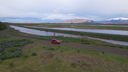 Wall Mural - 4X4 car driving on a country road in Þjórsardalur valley, along the river Þjorsa, Holtasoley flowers field, nearby the Burfell (Pjorsardal) and Hekla volcano in Iceland.