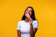Young Indian woman eating pink popsicle on yellow background. Asian woman eating ice cream. Looking at camera.