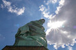 A view from under an iconic representation of freedom and independence, the Statue of Liberty with flaming torch on Liberty Island. The Lady on a Pedestal is surrounded by clouds. American history.