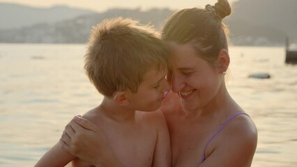 portrait of smiling boy hugging and having fun with his mother on sea beach at sunset. holiday, summ