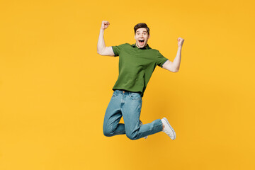 Wall Mural - Full body young overjoyed excited cool happy man he wears green t-shirt casual clothes jump high do winner gesture clench fist isolated on plain yellow background studio portrait. Lifestyle concept.