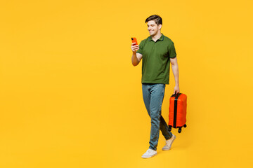 Traveler happy man wear green casual clothes hold suitcase mobile cell phone isolated on plain yellow background Tourist travel abroad in free spare time rest getaway. Air flight trip journey concept.