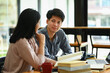 © Prathankarnpap - Asian male and classmate sitting at table preparing for exams finding information for their college assignment