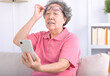 Presbyopia, senior asian woman holding eyeglasses having problem with vision problem trying to read text on mobile phone