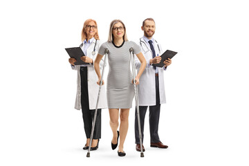 Wall Mural - Young female patietn with crutches standing in front of a male and female doctors