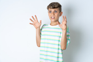 Wall Mural - Beautiful kid boy wearing striped casual t-shirt afraid and terrified with fear expression stop gesture with hands, shouting in shock. Panic concept.