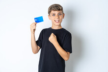 Excited Happy Positive Cheerful Smiling Beautiful Kid Boy Wearing Black Casual T-shirt Hold Credit Card Raise Fist In Victory