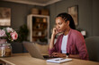 © bnenin - A pretty African female freelancer looking at the laptop screen and working from home.