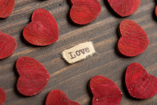 Love - typed text. Valentines Day greetings concept. Little red wooden hearts close up. Valentines greeting card.