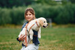 © standret - Holding animal in hands. Cute little girl is with golden retriever dog on the field
