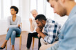 © dikushin - Side view of sad pensive young African American man talking about mental state sitting in circle during group therapy session. Concept of mental health, psychotherapy, social issues, support