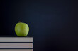 Stack of books with green apple and clean blackboard