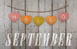 Hello September written on hanging yellow, red and orange hearts and weathered wooden background
