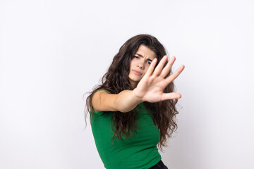 Portrait of a serious young woman showing stop gesture with her palm over white background