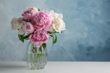 Sticker - Beautiful peonies in glass vase on white table. Space for text