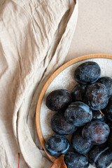 Wall Mural - Ripe plums on plate on linen neutral beige tablecloth background, aesthetic fruit flat lay