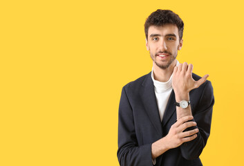 Wall Mural - Young man in suit with wristwatch on yellow background