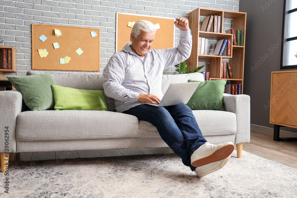 Happy senior man using laptop on sofa at home