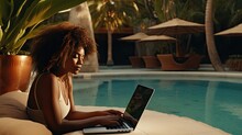 Young black woman working remotely on her laptop beside a pool, concept of freedom as a digital nomad and entrepreneurship