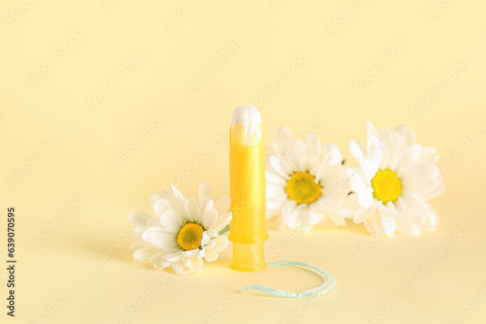 Menstrual tampon and beautiful chamomile flowers on color background