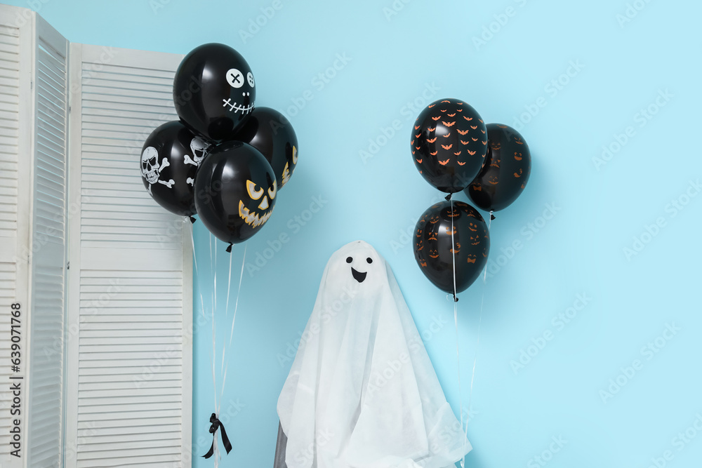 Different black Halloween balloons, folding screen and ghost near blue wall in room