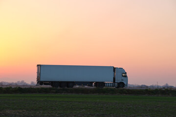 Wall Mural - Semi-truck with cargo trailer driving on highway hauling goods in evening. Delivery transportation and logistics concept