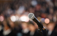 Close Up Of A Microphone On Stage With A Burred Bokeh Audience Or Crowd. Public Speaking Performing Nervousness Or Anxiety Theme