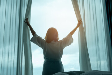 Wall Mural - In the morning, a woman opens the curtains of the window in the bedroom. woman stretching at the window health and care concept