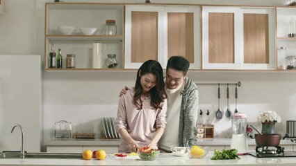 Wall Mural - young asian couple chatting while preparing meal in kitchen at home