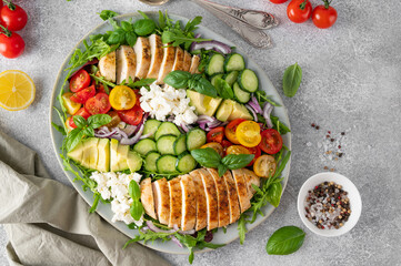 Wall Mural - Salad with roasted chicken, avocado, cherry tomatoes, cucumbers, arugula and feta cheese on a plate on a gray concrete background. Healthy food.