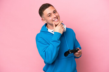 Wall Mural - Young brazilian man playing with a video game controller isolated on pink background happy and smiling