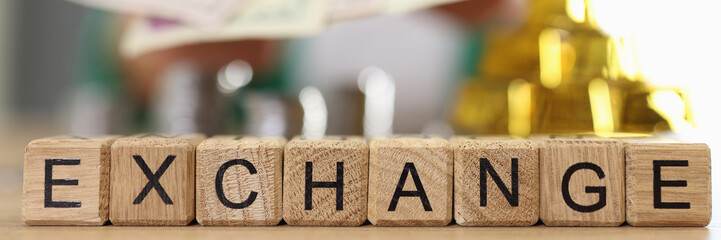 Wall Mural - Wooden cubes with word exchange and blurred gold bars, coins and person with dollars in background