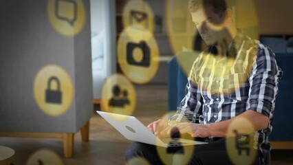 Poster - Animation of icons and computer language over caucasian man sitting on chair and working on laptop