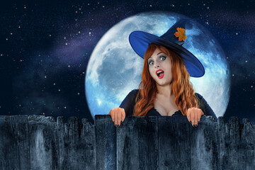 Halloween Witch peeking out behind a fence or wooden wall. Female wizard fairy character. All Saints' Day. Fantasy gothic red-haired sorceress girl dressed in black carnival costume