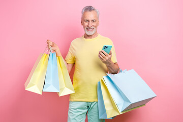 Wall Mural - Photo of clever senior man with beard dressed yellow t-shirt hold new clothes make order in smartphone isolated on pink color background