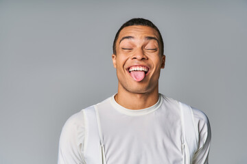 funny african american man in trendy t-shirt, with closed eyes, sticking out on grey background