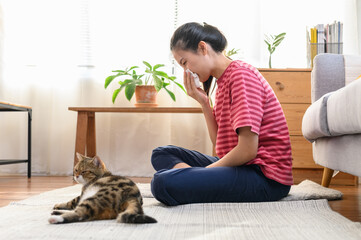 Young Asian woman sneezing which suffering from first symptoms of cat's fur allergy. Cute cat and allergic girl. Animal allergy people health illness concept.