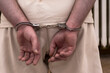Mężczyzna z rękami na plecach zapiętymi kajdankami . Aresztant , więzień, zatrzymany w białym płuciennym stroju w 