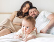 © Alexandra - happy young family with baby infant kid boy sitting on bed, cuddling kissing child on hand, cheek, caresses. traditional family lying on bed at home.woman man kid portrait,posing in bedroom