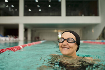 Wall Mural - cheerful middle aged woman in swim cap and goggles swimming in pool, water, recreation center, spa