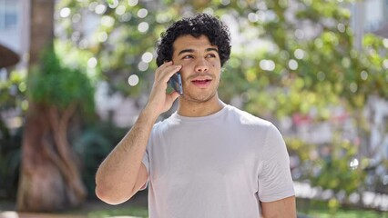 Sticker - Young latin man talking on smartphone looking watch at park